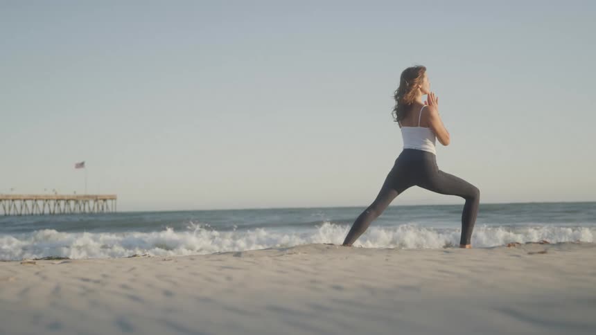 The woman does yoga on the beach as the waves hit the shore