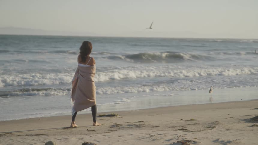 Woman walking on the beach sand with a scarf