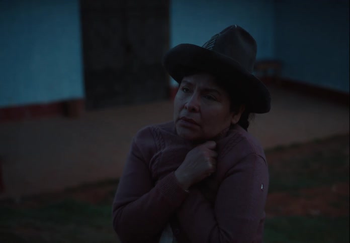 Woman wearing a hat and sweater hugs herself to stay warm outdoors at dusk