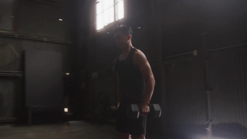A man is doing bicep curls with dumbbells he is wearing a black tank top and black shorts