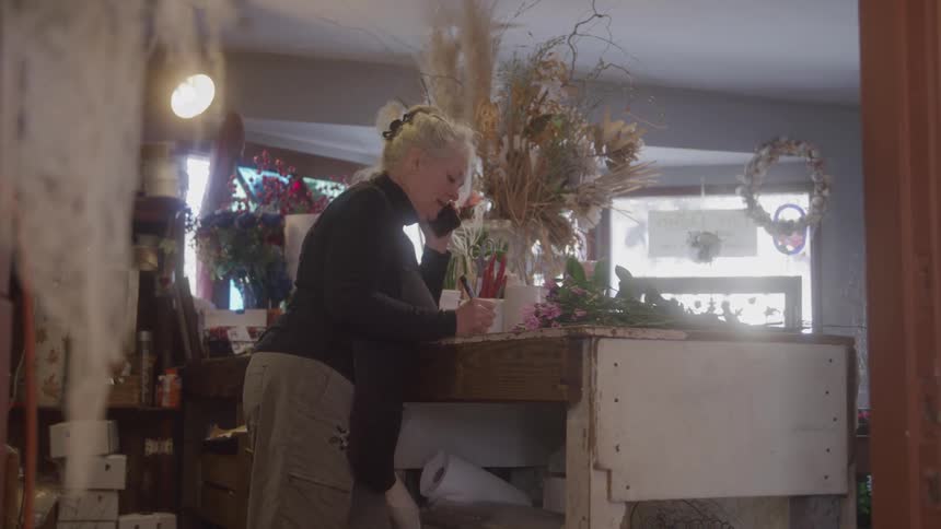 Florist talks on the phone while jotting down orders among arrangements