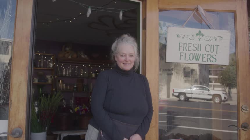 A woman stands smiling in front of a flower shop