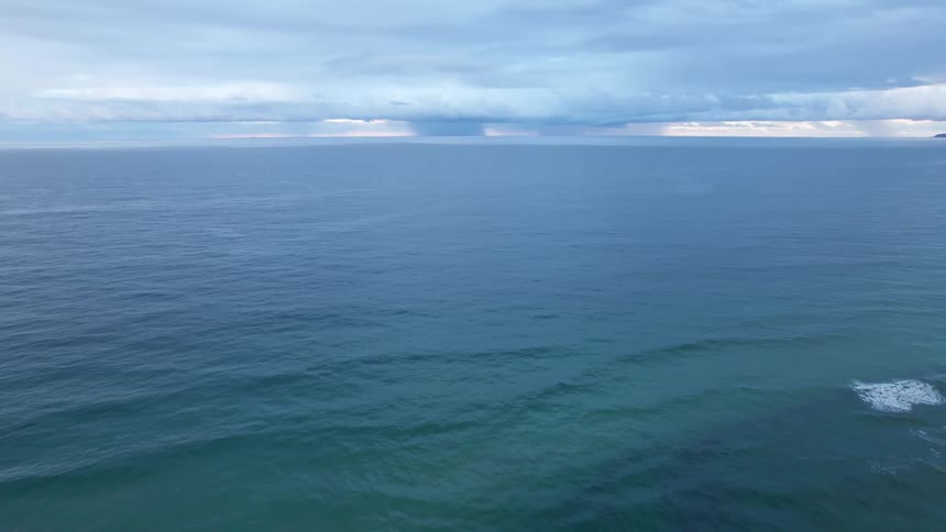 Waves move across the surface of the ocean under a cloudy sky