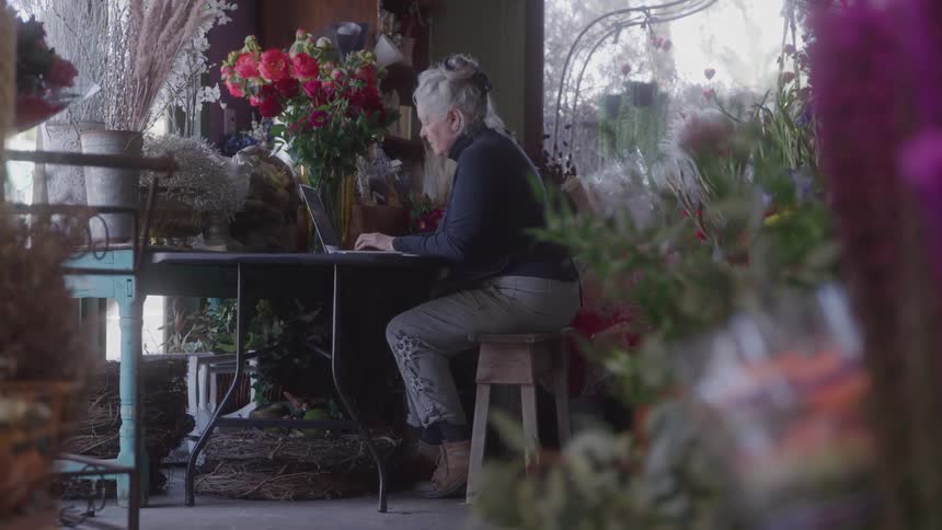 The woman in the flower shop is using a laptop