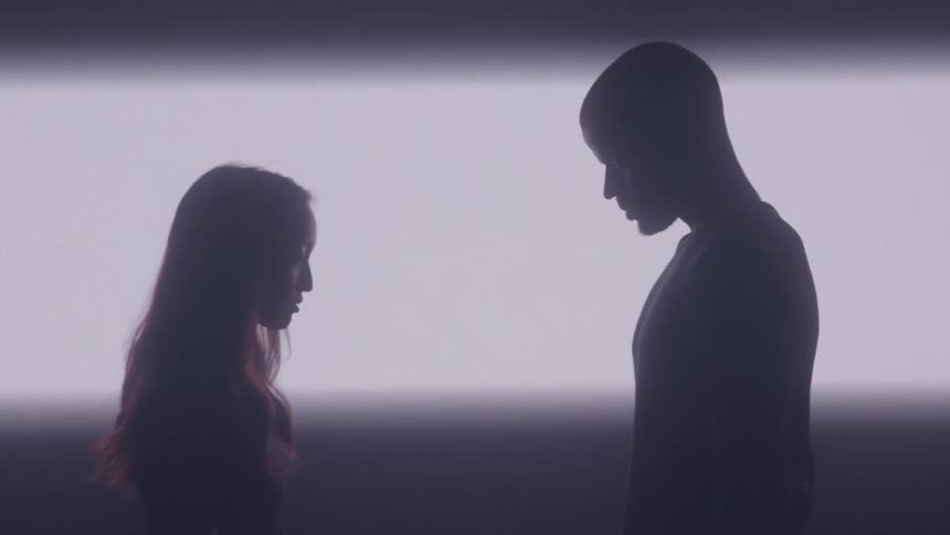 Silhouettes of a man and a woman face to face before a white light that fades in the background