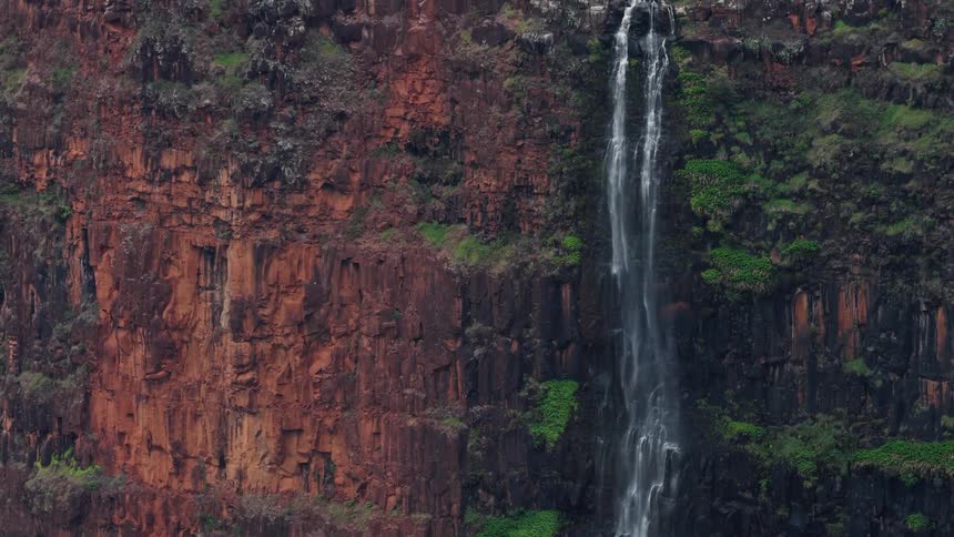 A mountain with a stream flows down its slope creating a waterfall at midday