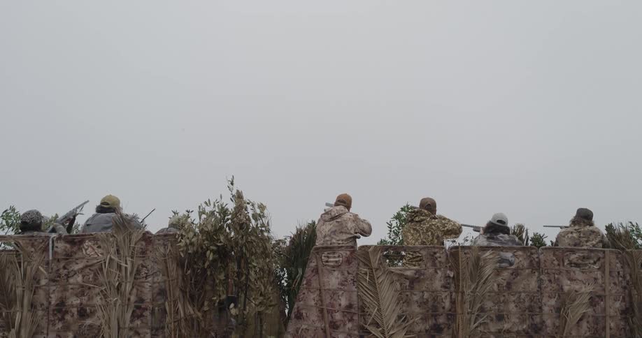 Group of men in camouflage clothing holding guns behind a foliagecovered barricade