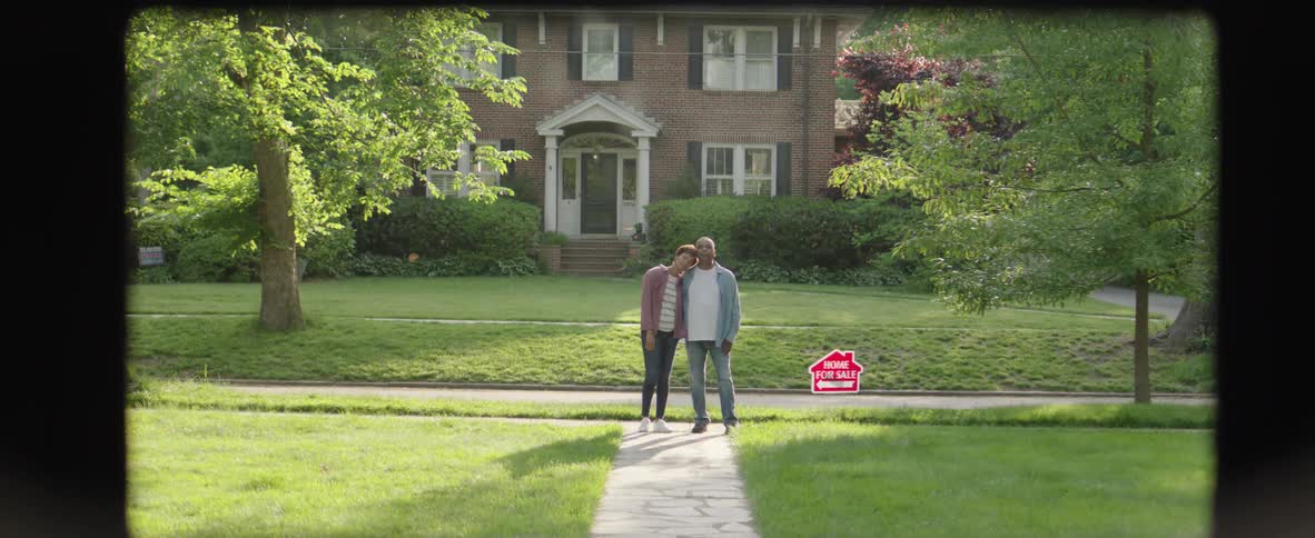 Couple smiles in front of a house for sale
