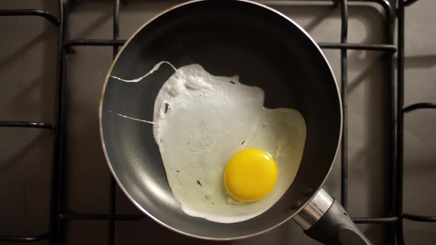A mans hands crack an egg into a frying pan on the stove