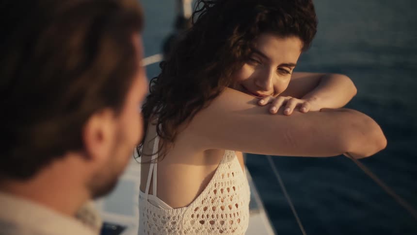Woman smiling and resting her arms on a boat railing while looking at a man in front of her