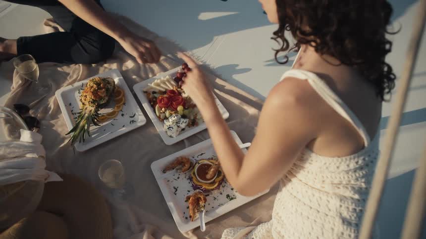 A person is being served food and drinks on a boat deck the man is seated with a woman out of focus to his right