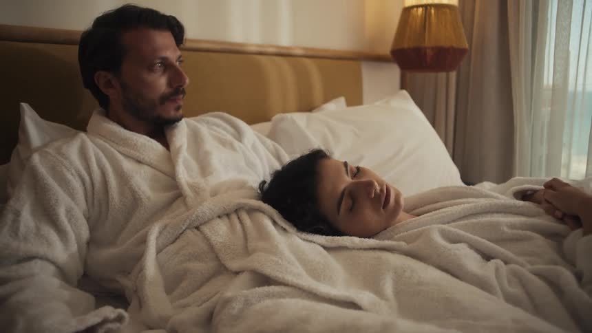 Man and woman in bathrobes resting together in bed