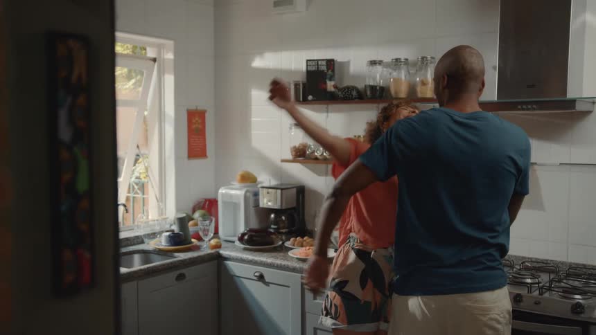 A man and a woman are in a kitchen smiling and laughing together the woman is seen walking towards the man and they share a hug