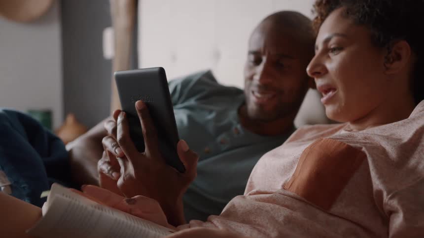 A couple is relaxing together with the woman holding an ereader or tablet they are both smiling and looking at the screen