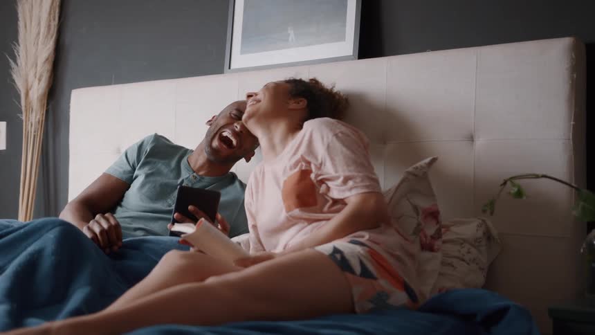 A couple is sitting on a bed in their bedroom laughing and having fun together