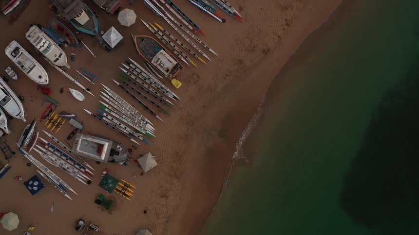 A series of boats are docked on the sandy beach at midday