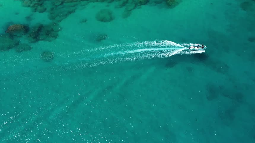 Small boat traveling around an island with turquoise blue water