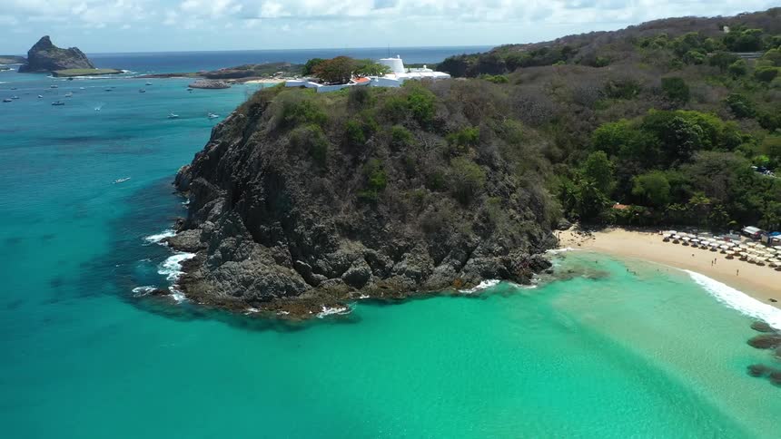 Aerial view of a beach with turquoise sea and a treecovered cliff