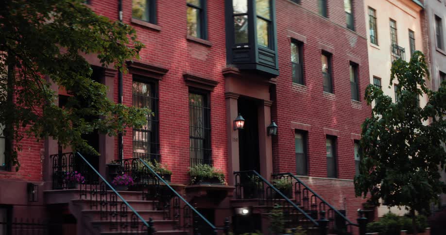A stationary shot of the exterior of a classic brick row house with a bay window and front steps leading to the door