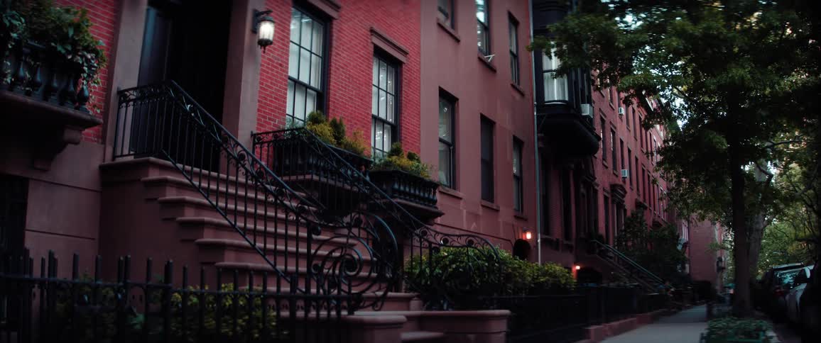 A closeup of a residential street shows the exteriors of two red brick townhouses in a quiet upscale neighborhood