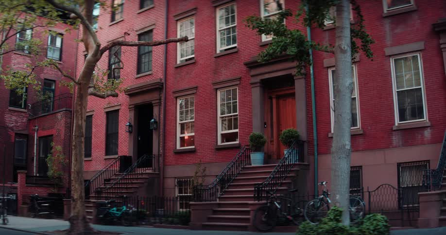 A steady shot of a red brick townhouse with a green tree on the sidewalk