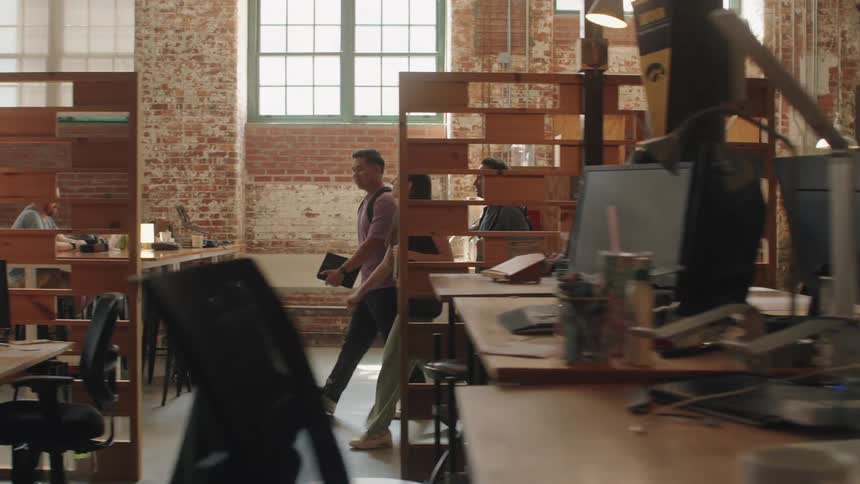 Three people walk through a warehouse filled with a series of cubicle offices at midday