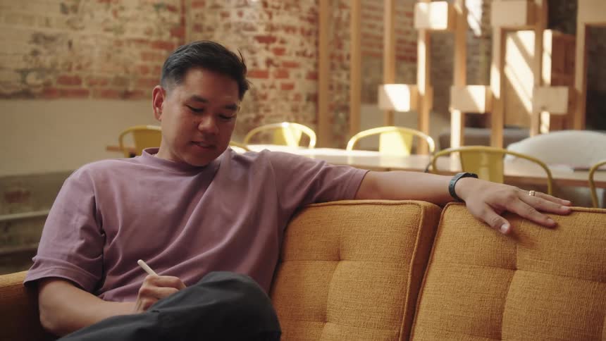 Asian man takes notes while sitting on a couch and talking