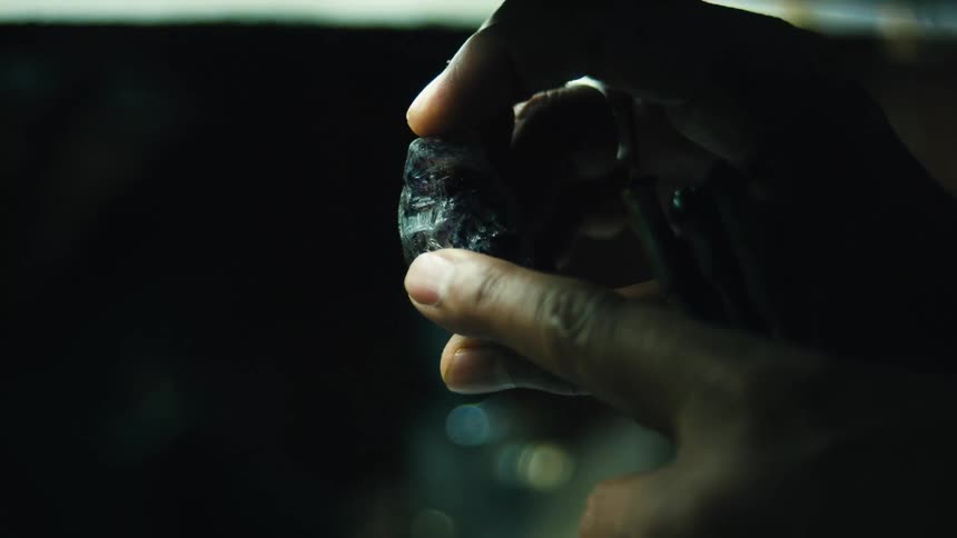 A person examines a rough dark gemstone