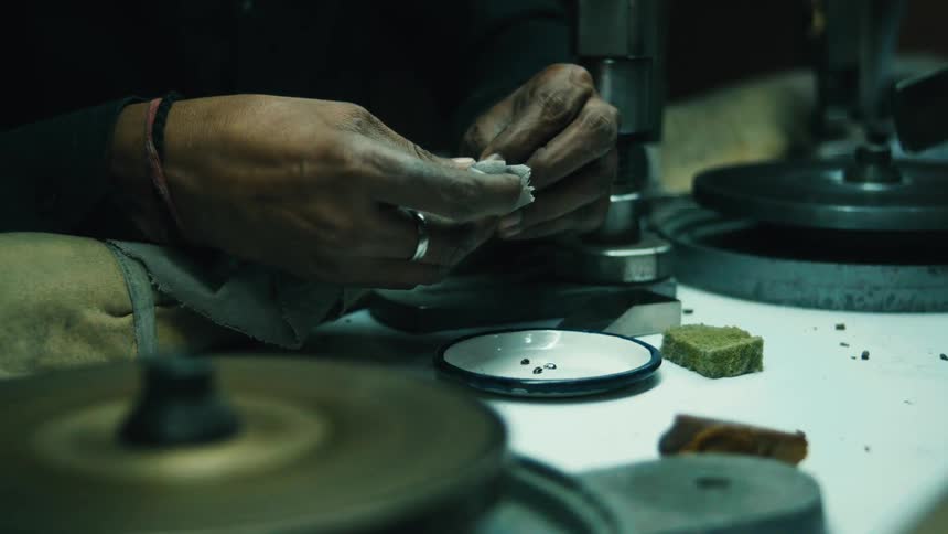 Hands carefully handle small stones or gems at a workbench with precision tools