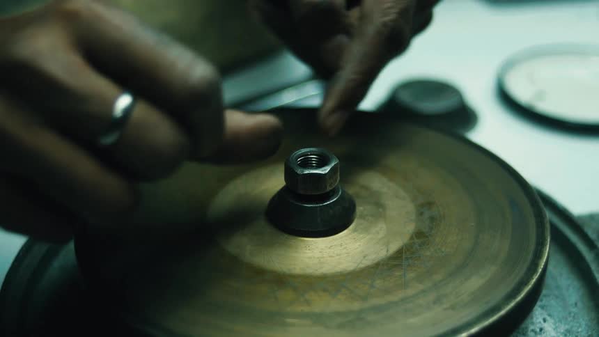 A shot of a persons hands as they use a wrench to loosen a bolt on a piece of machinery they then remove the bolt and the attached piece before examining a ring on their finger and pointing to the machine