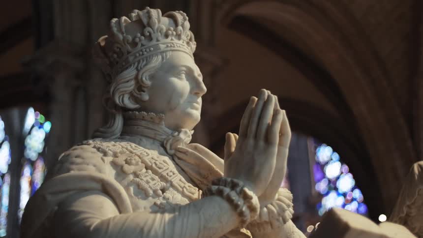 Statue of a king with a palm of his hands together inside a cathedral