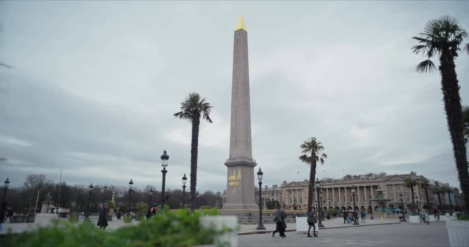 The luxor obelisk stands in the streets of paris at midday as people walk by