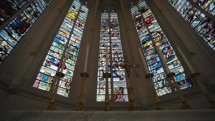 A church altar with tall artistic windows behind it and a series of candles placed on top of the altar