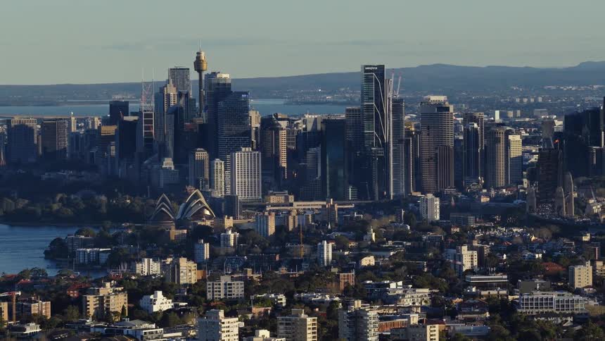 The iconic sydney skyline featuring the opera house and sydney tower is bathed in the warm glow of the sun