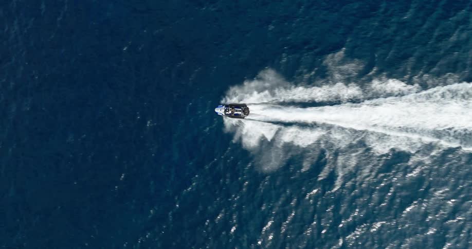 The video shows a highangle shot of a person on a jet ski moving at high speed across the water the jet ski creates a large white spray and wake behind it