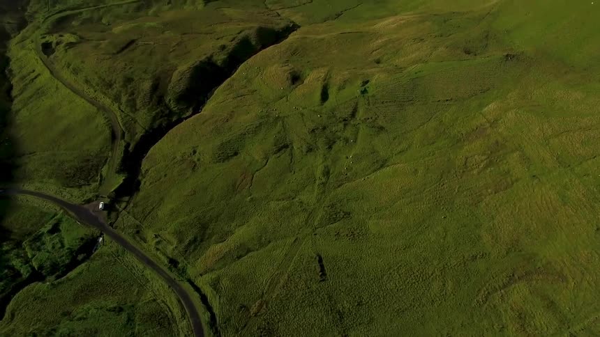 An overhead view of a large green field with a run down building in there