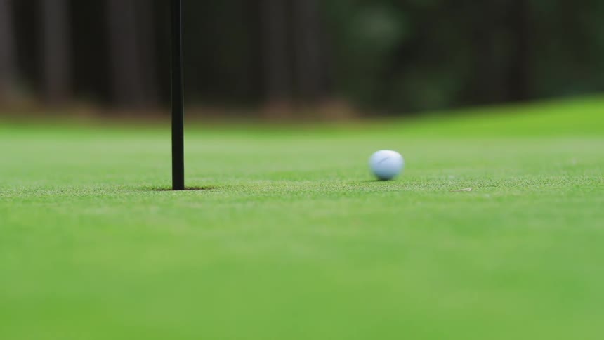 The golf ball slowly rolls towards the hole