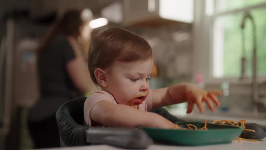 Baby sitting eating pasta with sauce with her hands