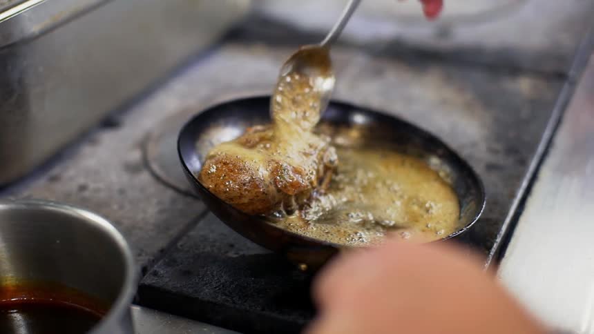 A chef bastes a cut of meat in a skillet