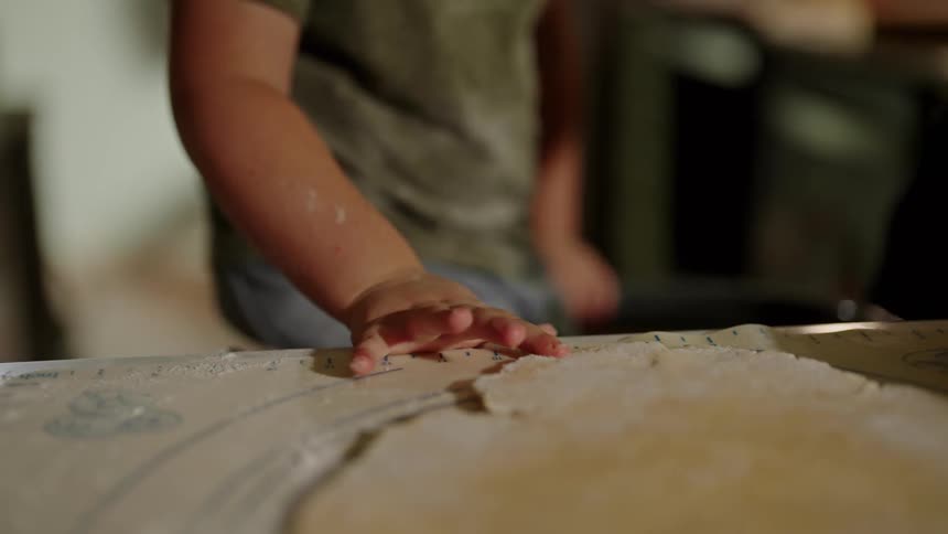 A child hand presses dough on a floured surface