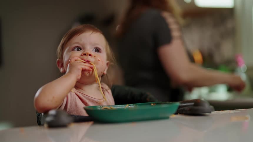 Toddler self feeding noodles at a table