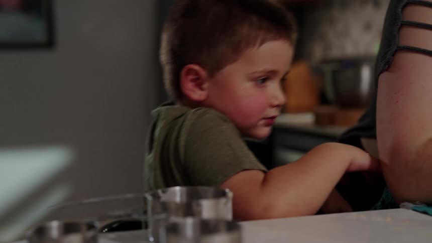 A young boy leans on a kitchen counter while looking toward someone nearby
