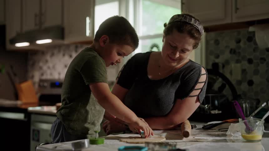 A child and an adults hands are shown working together to cut out cookie dough shapes on a floured countertop