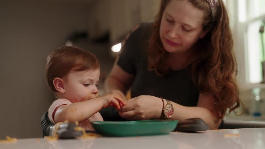Woman helping a baby eat pasta at a table