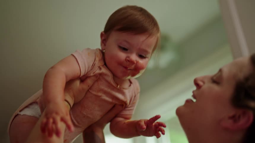 Mother kissing her little daughter on the cheek who is covered in pasta sauce