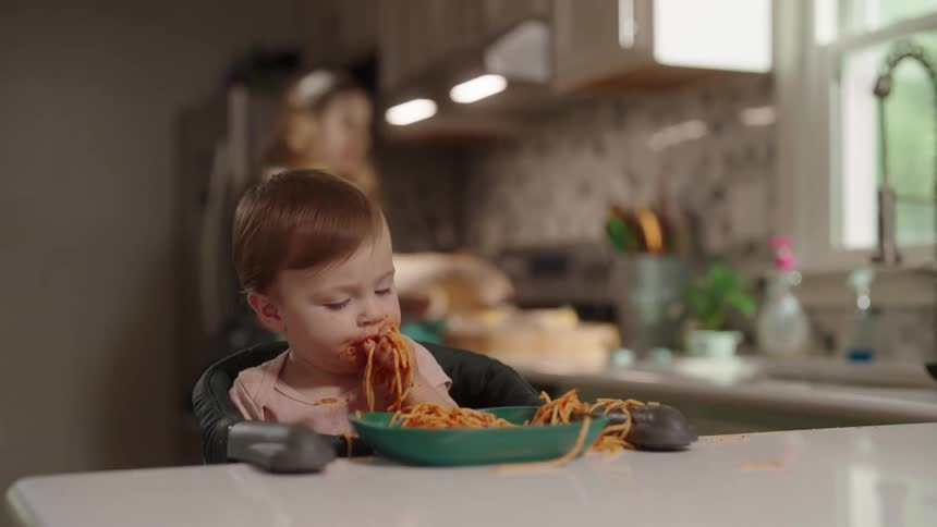 A toddler eats spaghetti at a kitchen counter