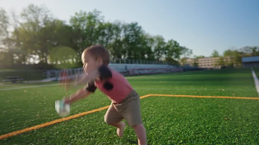 Little boy learning to walk and falling on artificial grass while holding a toy in his hands