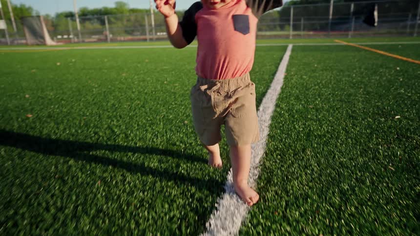 A little toddler boy learning to walk along a soccer field white line