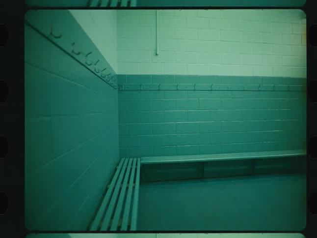 An empty locker room with teal and white tiled walls a wooden bench and a line of hooks