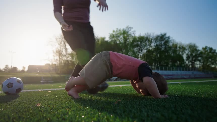 Mother helping to hold her son upside down in a grassy field